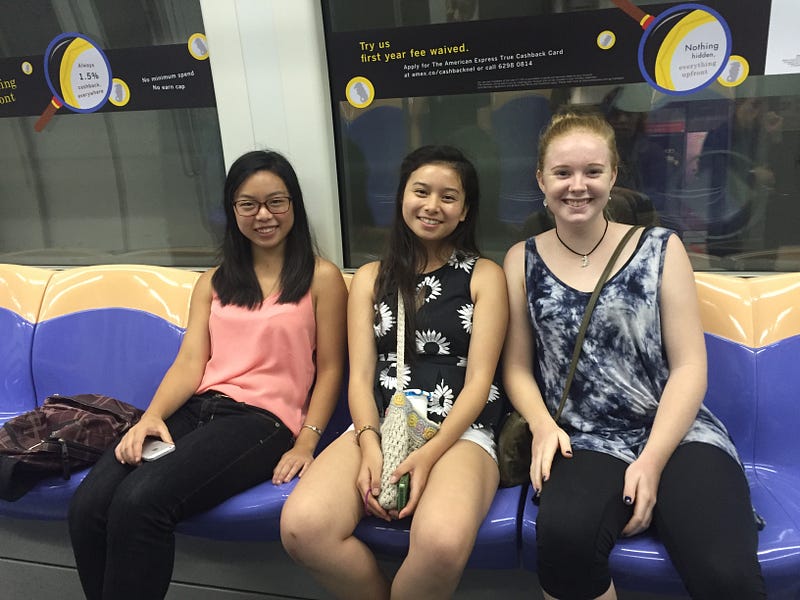 three students sitting on the metro looking at the camera, all smiling