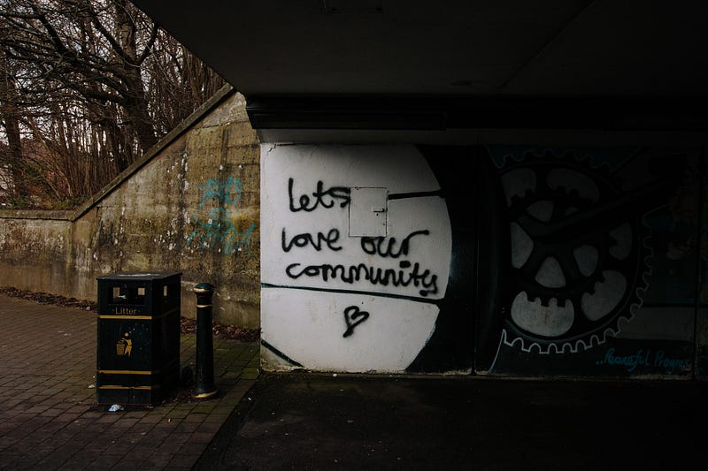 Picture of under a bridge where “Lets love our community” is written on the wall in spray paint.