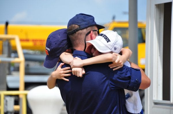 Military dad hugging his two kids with a semi-truck in the background.