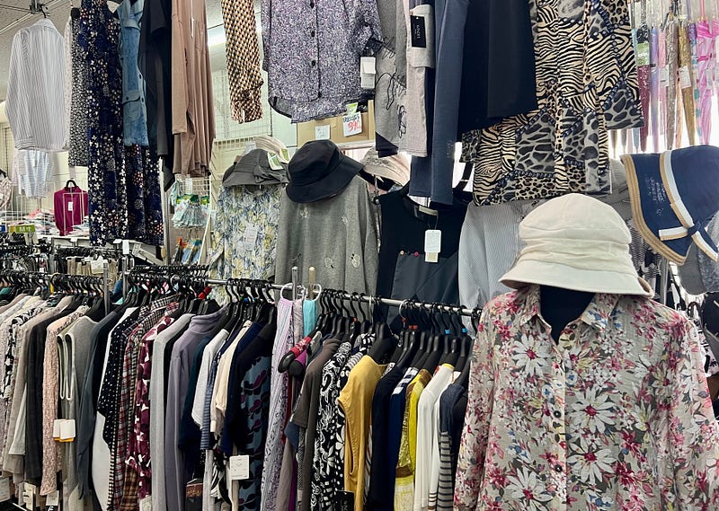 Rows of dull-colored clothing hanging on racks at a store. Older women wearing only dull colors is a weird Japanese thing.