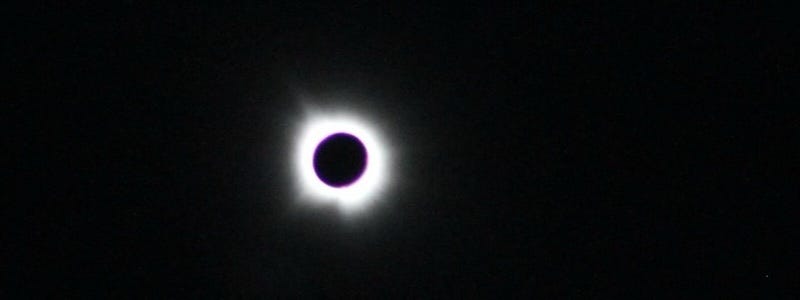 The circle of the sun eclipsed by the moon over a black background with bright rays of light around it.