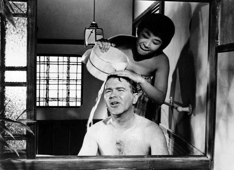 Cena em preto e branco do filme Sayonara. Nela, Red Buttons encontra-se em uma banheira, enquanto Umeki, enrolada em uma toalha, joga água na cabeça dele.