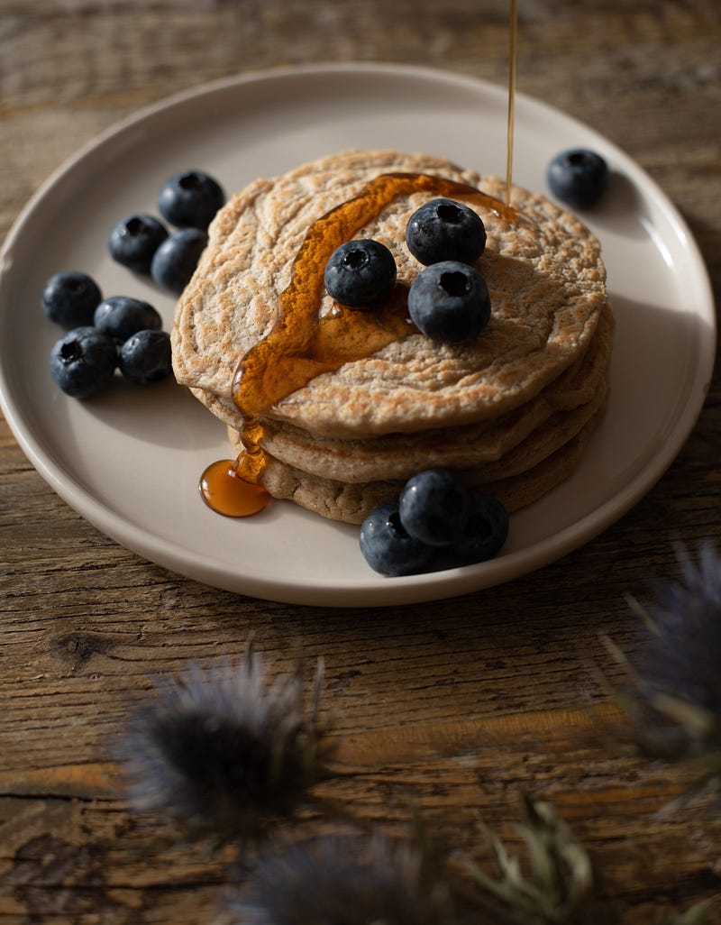 A stack of whole-wheat pancakes with blueberries and a drizzle of maple syrup.