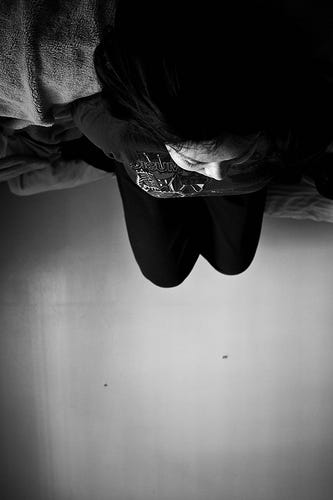 Description: This is a black and white photograph, taken upside down, of a person lying in a bed, looking at a blank wall.