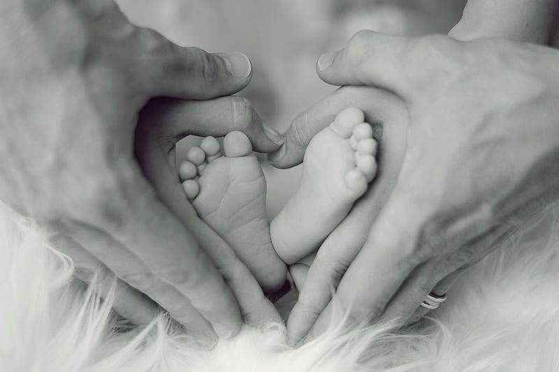Newborn feet nestled within a heart shape created by mom and dad’s hands