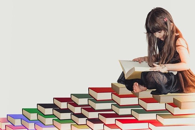 Girl reading while sat on many books.