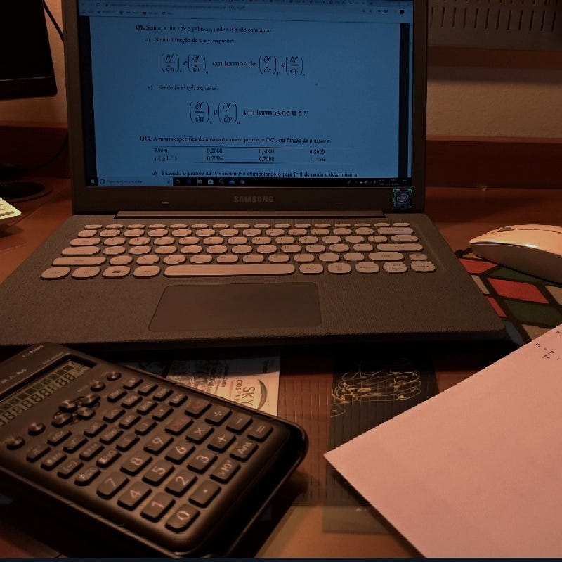 Uma mesa de estudos: notebook, calculadora e anotações.