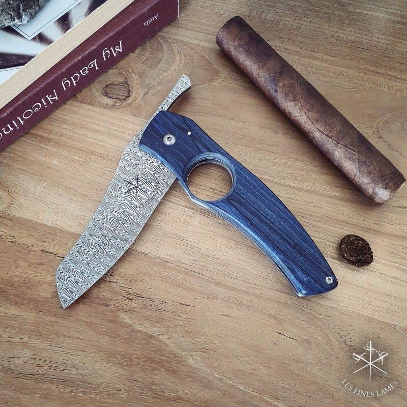 Les Fines Lames Cutter in Blue with Damascus Steel displayed next to a cigar that has just been cut
