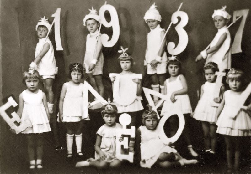 A group of small children dressed as angels, holding paper digits 1937 and letters