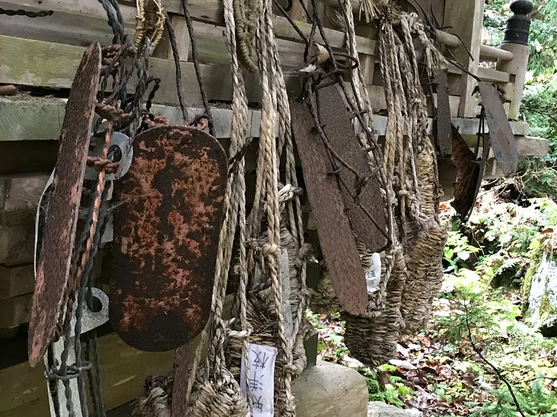 Rusted iron sandals and straw sandals hanging on the side of a wooden shrine building.