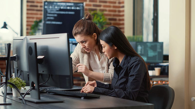 Two women programmers looking at two monitors, trying to explain something