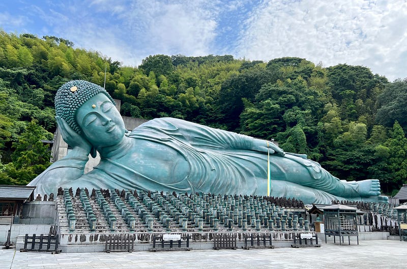 Reclining Buddha against a backdrop of green leafy trees.