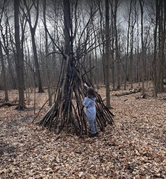 Young girl bulding tpee in woods out of sticks.
