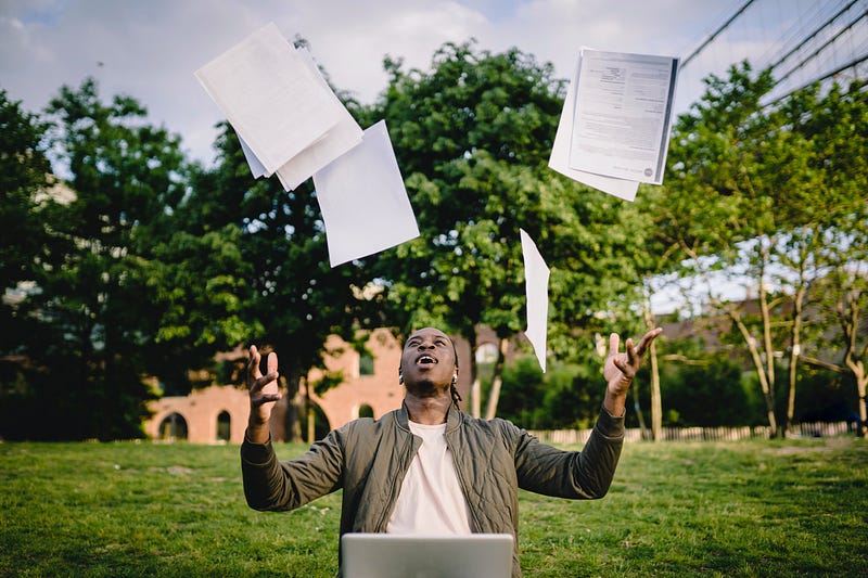 Man with his laptop at a park throwing papers in the air