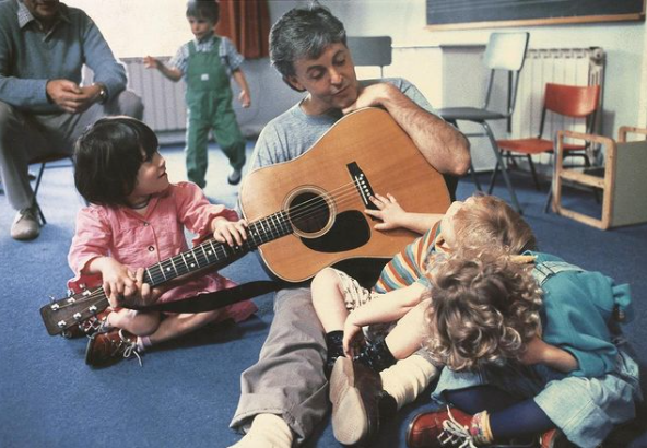 Paul McCartney with guitar visiting with children in 1986