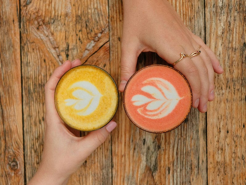 Two hands holding yellow and orange flavored drink in opposite directions.