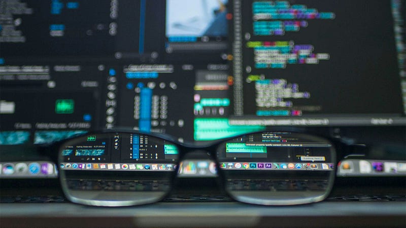 The image depicts a pair of eyeglasses in sharp focus in the foreground, resting on a keyboard. Through the lenses of the gla