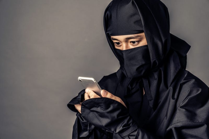 A ninja who is garbed in all black stares at a cellphone