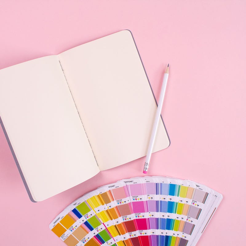 Photo of a notebook and printed Pantone colour cards sitting on a pink surface