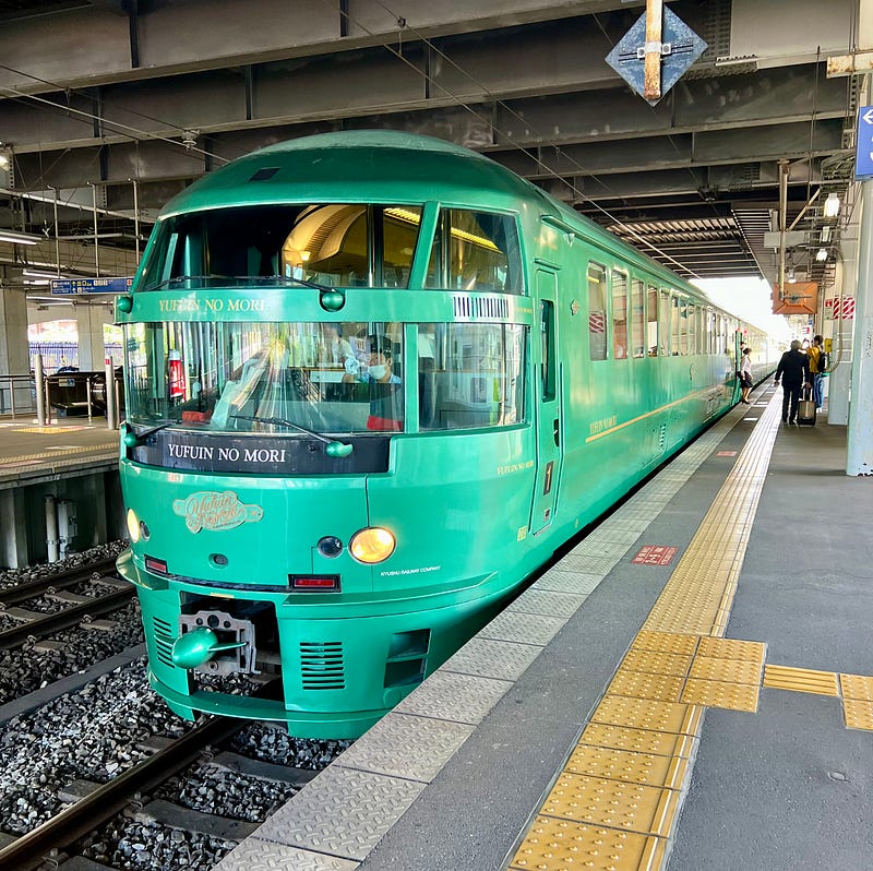 Beautiful green train with wide windows just pulled in at a train station.