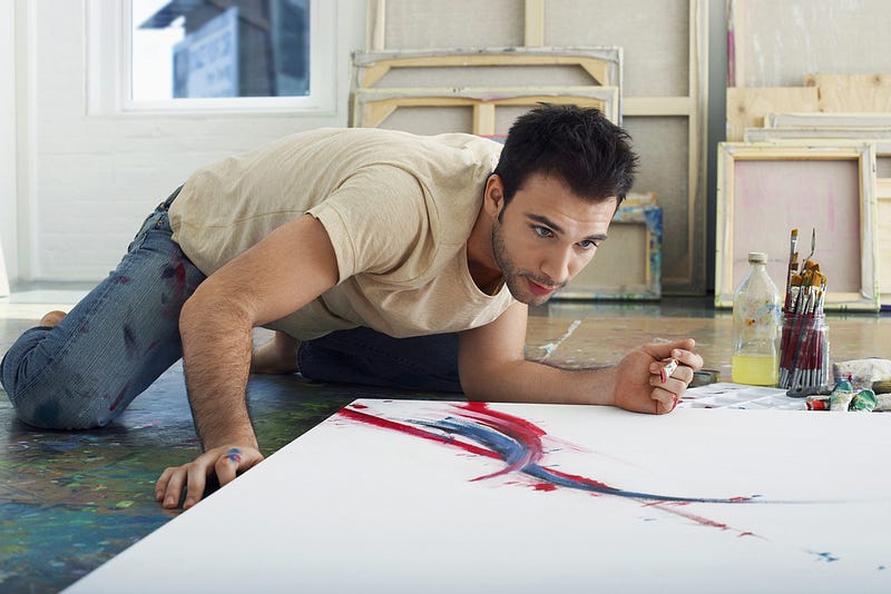 A man on the floor with his painting of abstract lines, brush in hand.