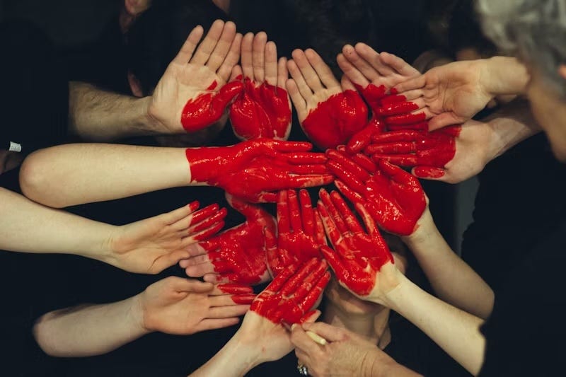 An image of several hands covered in red paint joined in a circle