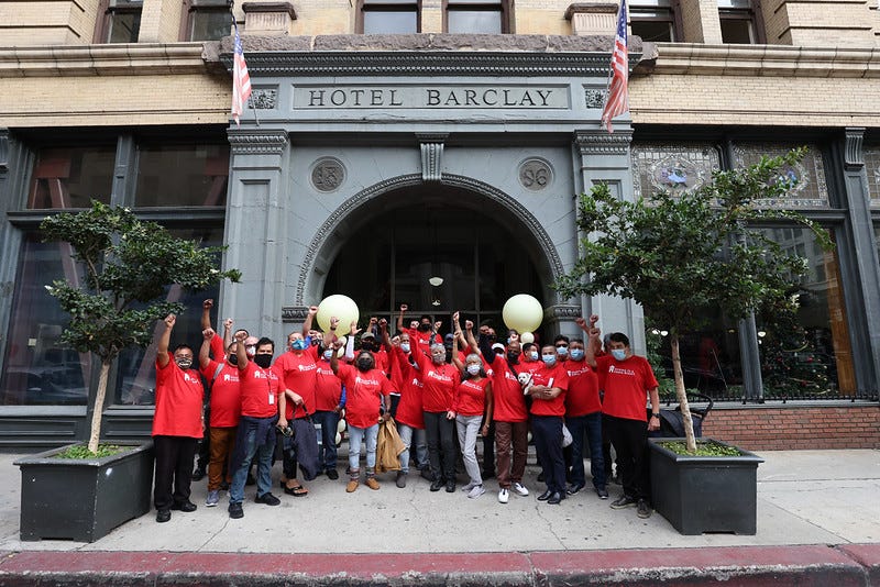 A group of people in red shirts with raised fists stand outside Hotel Barclay in downtown Los Angeles