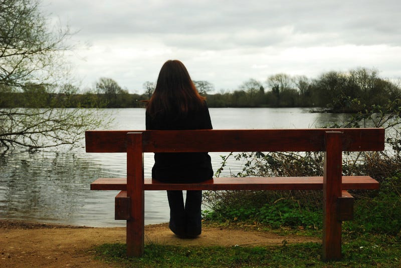 Woman sitting on bench alone in front of lake