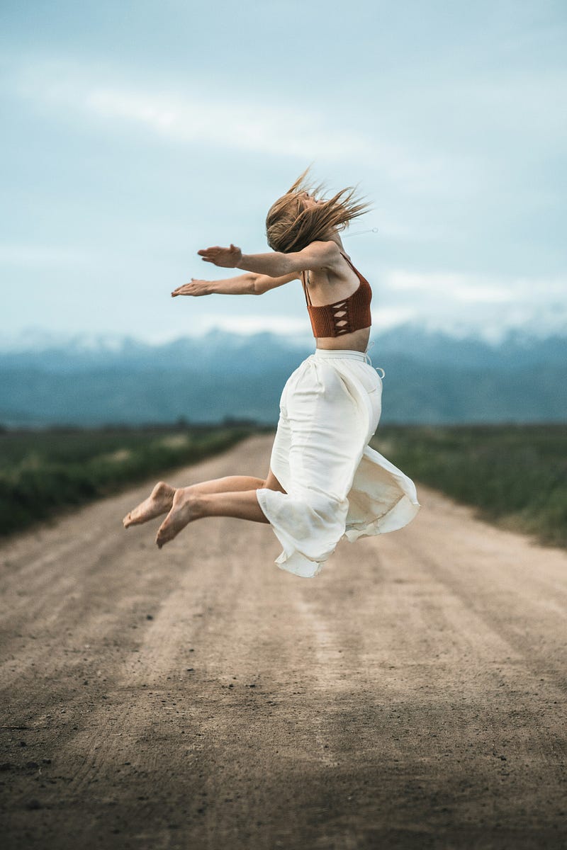 A woman jumping off the ground looking up, hands to the side and knees bent.