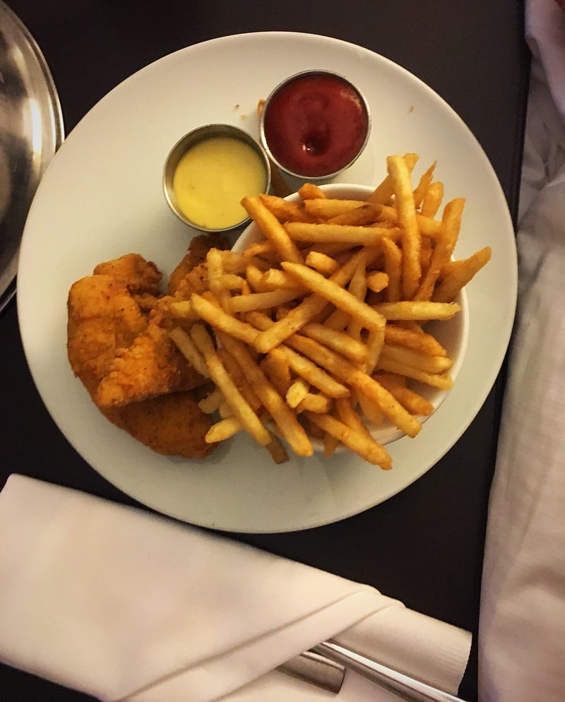 Chicken Tenders, fries, honey mustard sauce in a ramekin, ketchup in a ramekin, cloth napkin with silverware tucked inside