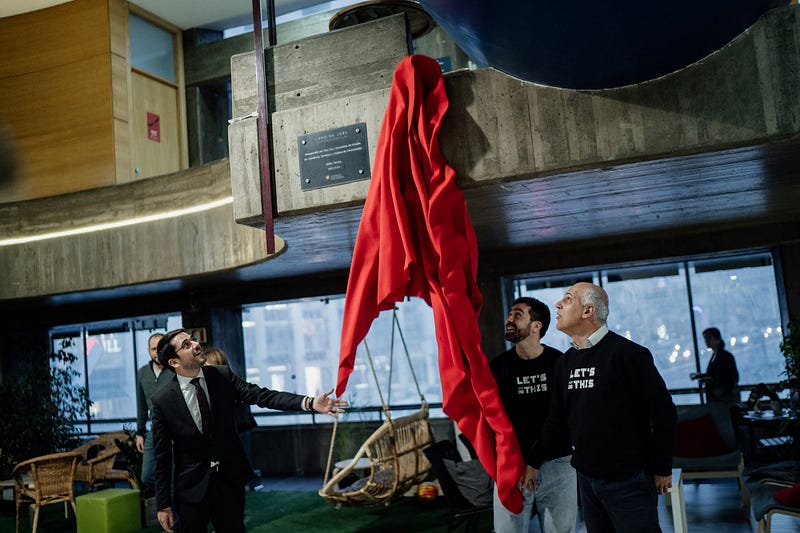 Three men unveiling a red curtain 