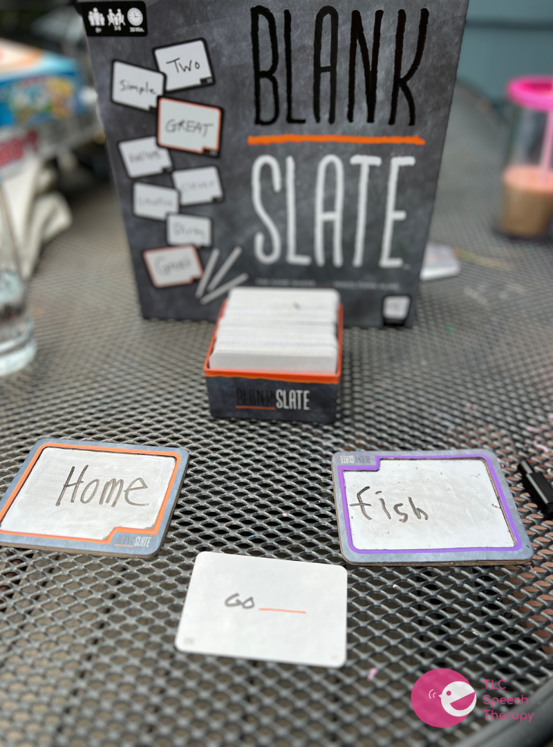 The game ‘Blank Slate’ is on a mesh table. The words ‘home’ and ‘fish’ are written on small dry erase boards for the prompt “Go _____”.