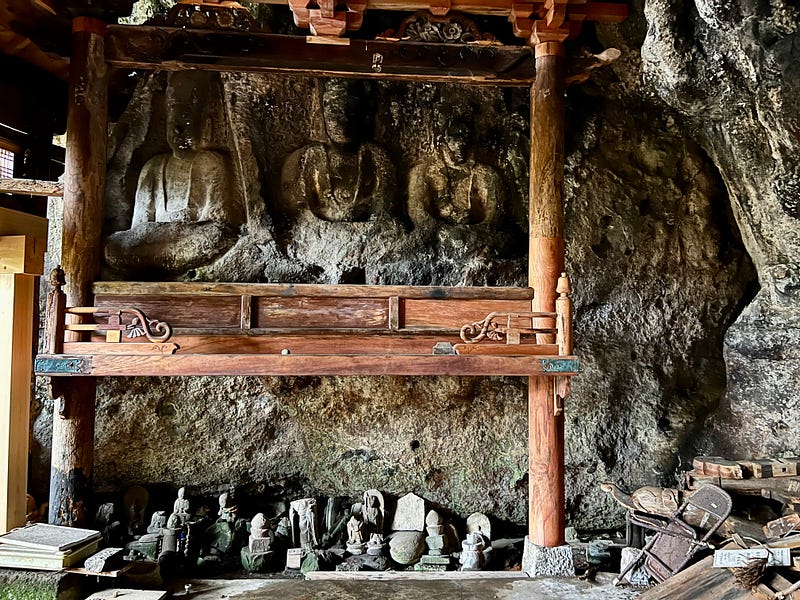Three Buddhist images carved into the cave wall with a wooden frame in front of them.