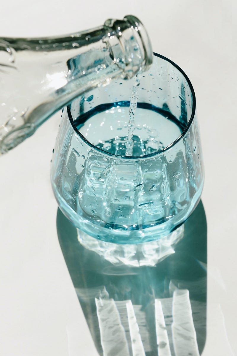 A clear glass bottle pouring water into a glass on a white surface.