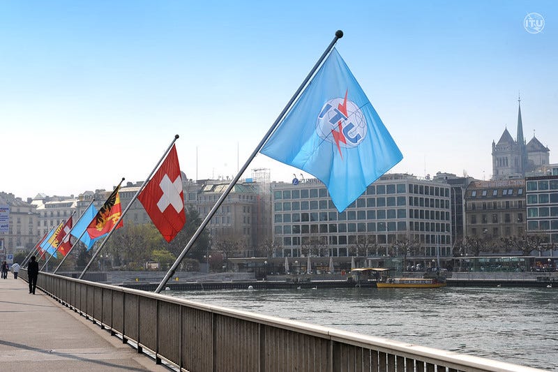 Flags, including the ITU flag, on poles over a river
