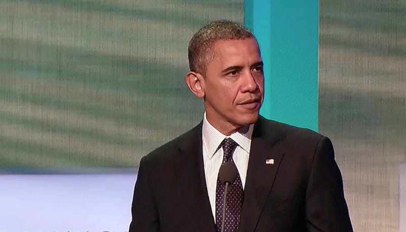 Photograph of President Obama giving a speech, wearing a black suit.