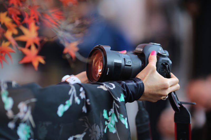 A woman in a kimono holds a DSLR camera for shooting koyo