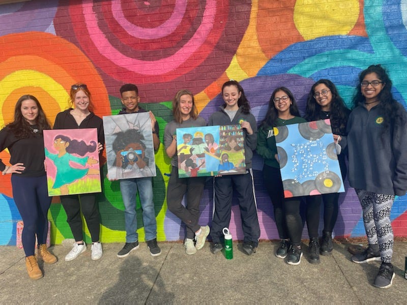 A group of Wayne State University Alternate Spring Break volunteers hold paintings and pose outside Mint Artists Guild’s Studio in Palmer Park, Detroit, Mich.