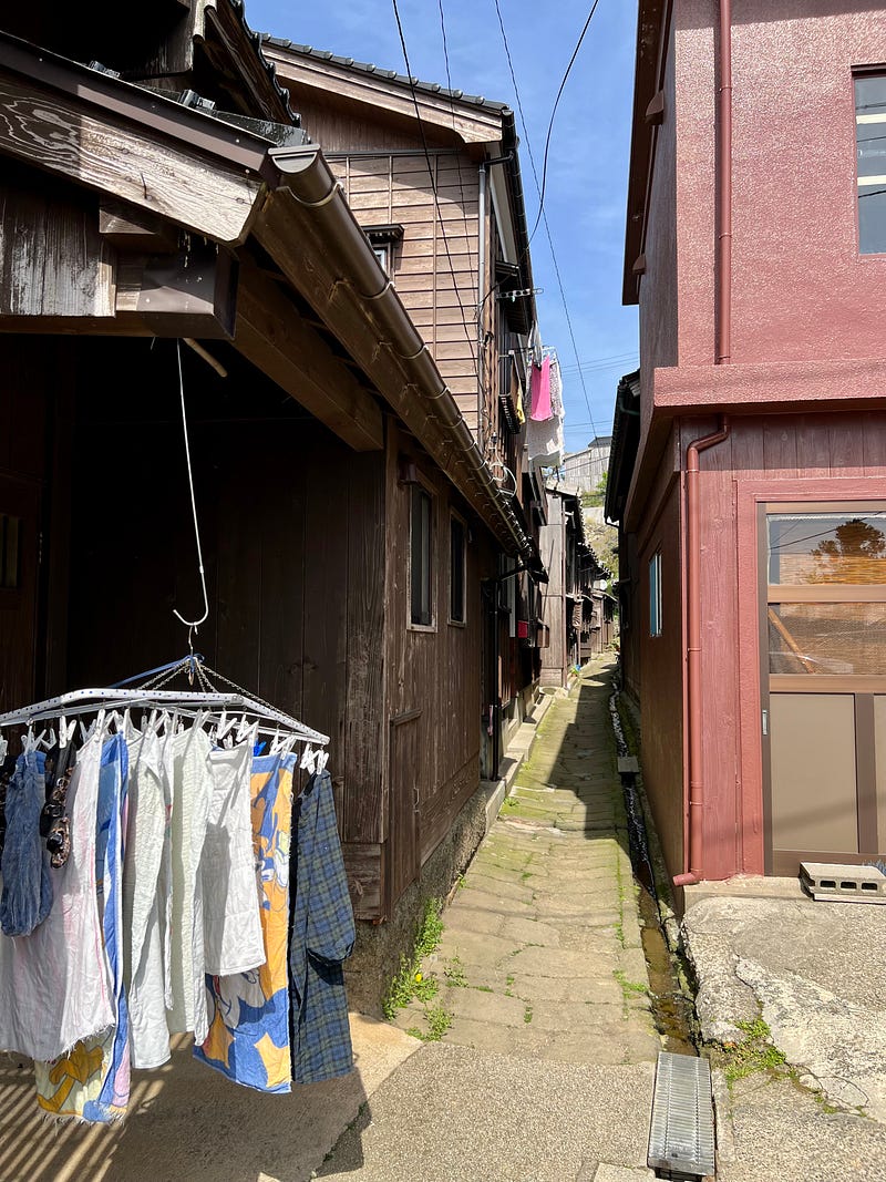 Very narrow walkway between buildings with laundry hanging from houses on the left in Shukunegi, Sado Island.