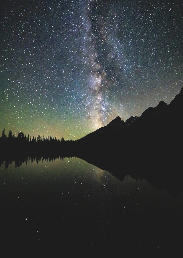 The Milky Way stretches across the night sky above String Lake in Grand Teton National Park, with starry reflections glowing on the still water — astrophotography by Dan Sproul.