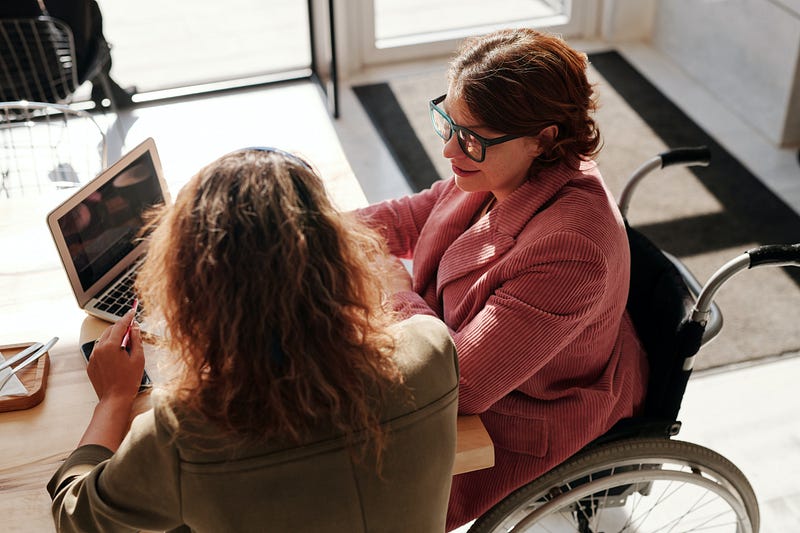 Two people sitting at a computer together and collaborating (Photo by Marcus Aurelius from Pexels)