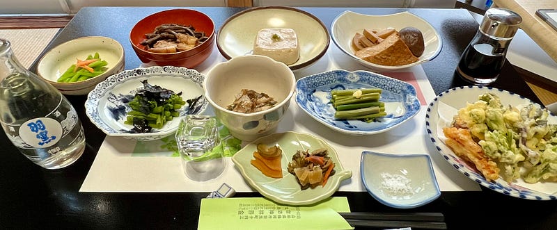Table covered with many small plates and bowls filled with vegetables and tofu.