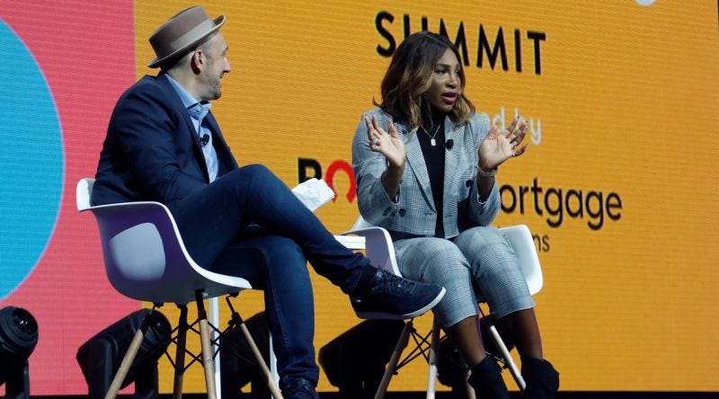 Serena Williams and a man sitting on two chairs on stage at the 30 Under 30 Summit, talking to a crowd out of frame.