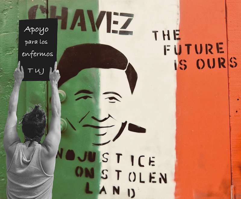 A woman holds a sign over her head. In the background is a mural of Cesar Chavez with the text segments: “Chavez,” “The future is ours.” and “No justice on stolen land.”