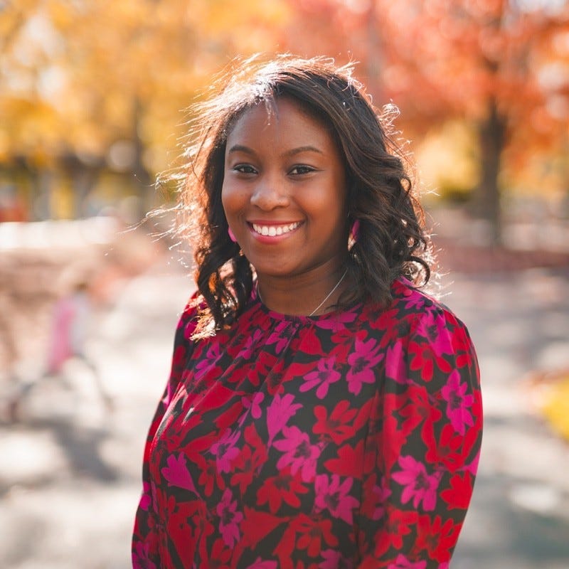 Natalie Cantave smiling with pink, red, and black flower shirt on.