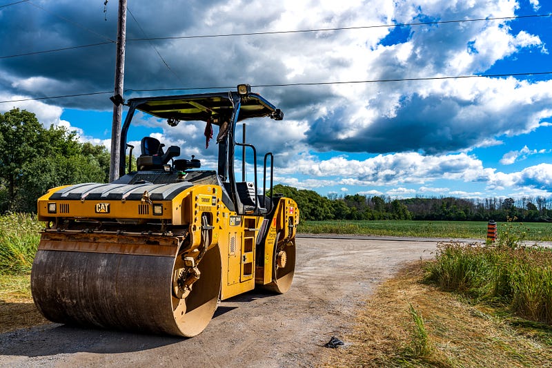 Steamroller on a dirt road against the backdrop of a blue sky.