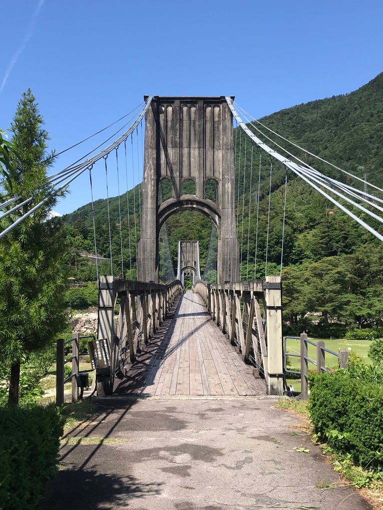 Wooden suspension bridge against a blue sky and green mountains.
