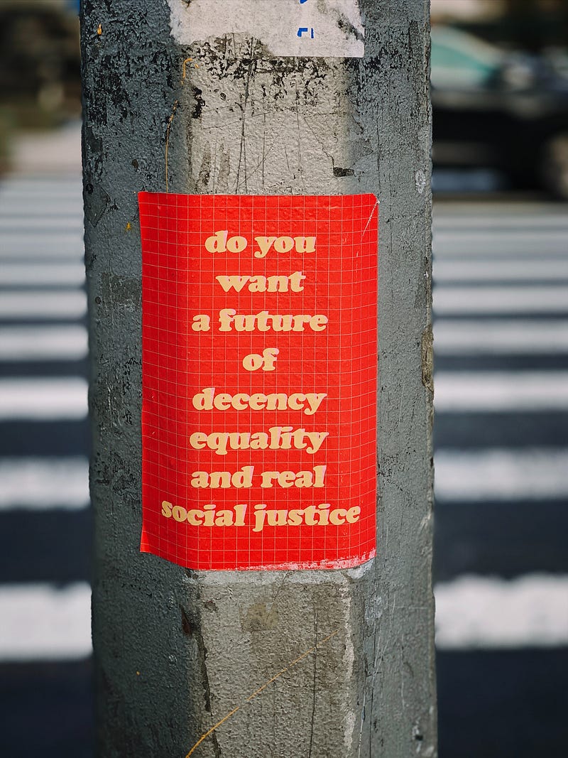 Picture of a sticker on a pole reading “do you want a future of decency equality and real social justice”