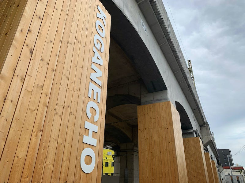 A sign reads “Koganecho” on a pillar that supports the overhead train tracks