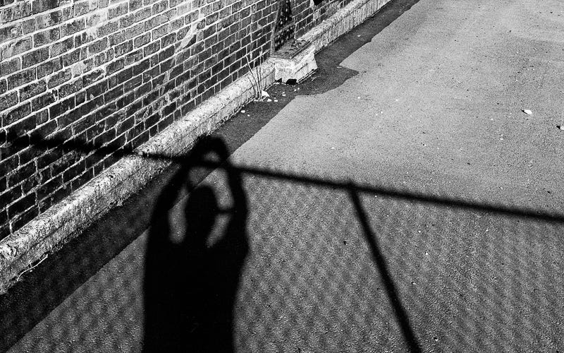 The shadow of a man leaning on a chain link fence.